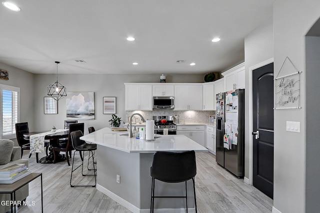 kitchen featuring a sink, light countertops, appliances with stainless steel finishes, a kitchen breakfast bar, and backsplash