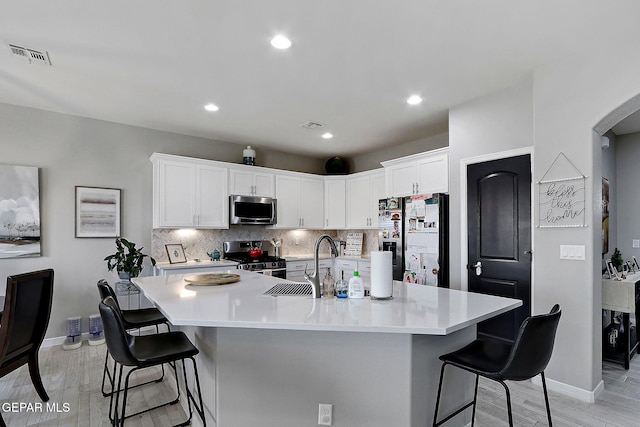 kitchen with visible vents, white cabinets, appliances with stainless steel finishes, a kitchen bar, and backsplash