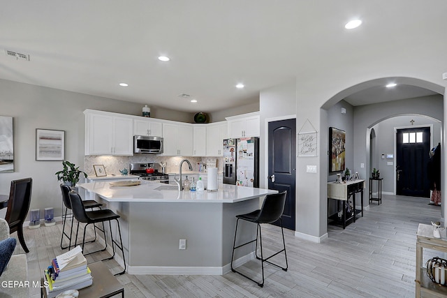 kitchen featuring tasteful backsplash, appliances with stainless steel finishes, a kitchen breakfast bar, white cabinetry, and a sink