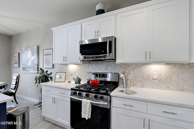 kitchen featuring tasteful backsplash, appliances with stainless steel finishes, white cabinets, light countertops, and baseboards