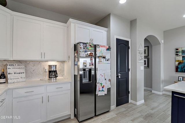 kitchen featuring arched walkways, light countertops, stainless steel refrigerator with ice dispenser, white cabinetry, and tasteful backsplash