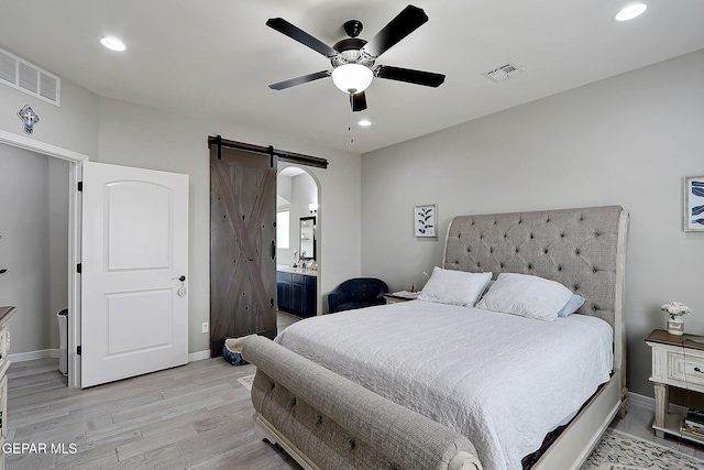 bedroom featuring visible vents, light wood-style flooring, baseboards, and a barn door