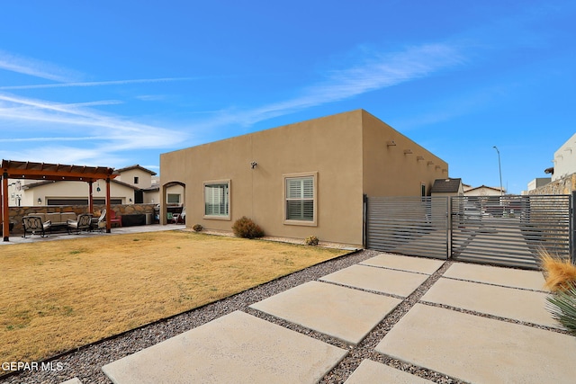 back of house featuring a gate, a patio area, a pergola, and stucco siding