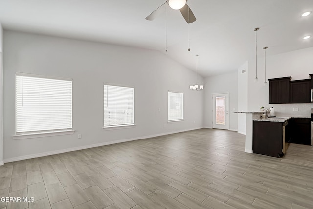 unfurnished living room with light wood-type flooring, high vaulted ceiling, ceiling fan with notable chandelier, a sink, and baseboards