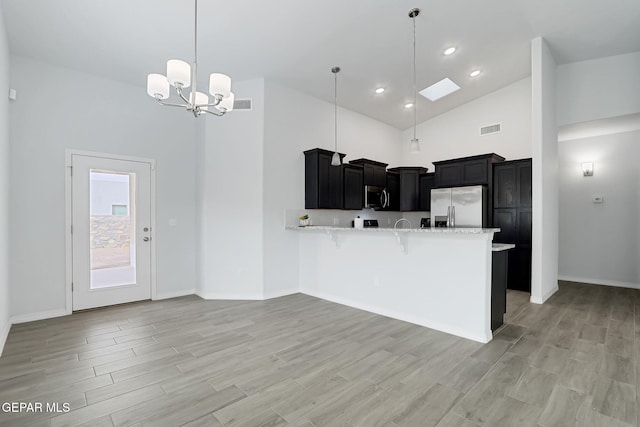 kitchen with a kitchen bar, appliances with stainless steel finishes, a peninsula, dark cabinetry, and high vaulted ceiling