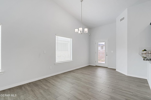 spare room featuring wood finished floors, baseboards, visible vents, high vaulted ceiling, and a chandelier