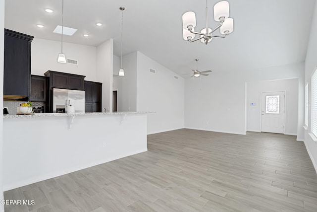 kitchen featuring a breakfast bar, ceiling fan with notable chandelier, light wood-style flooring, stainless steel refrigerator with ice dispenser, and hanging light fixtures