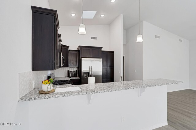 kitchen featuring visible vents, a breakfast bar, a peninsula, stainless steel refrigerator with ice dispenser, and gas stove