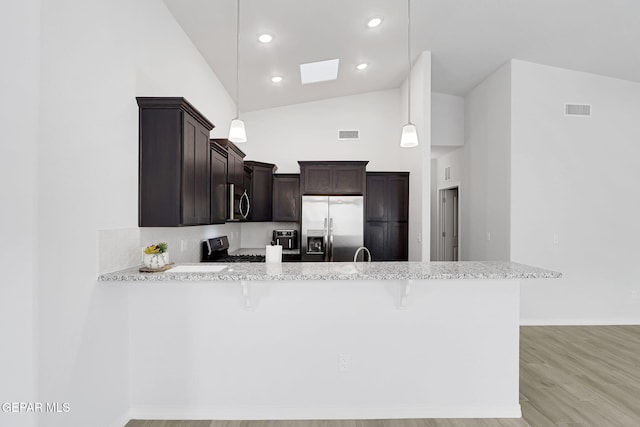 kitchen featuring visible vents, a peninsula, stainless steel appliances, dark brown cabinetry, and a kitchen breakfast bar