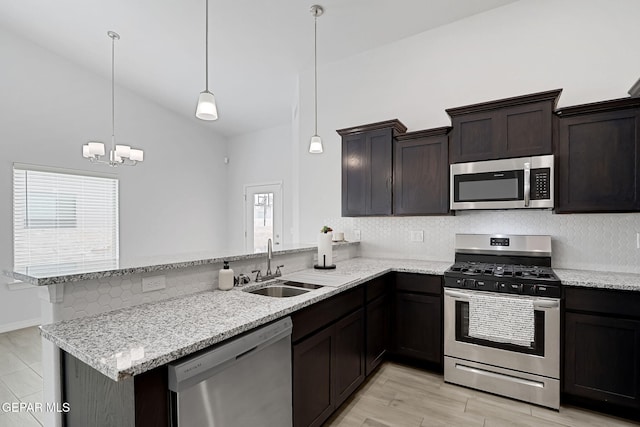 kitchen with a sink, light stone counters, dark brown cabinetry, appliances with stainless steel finishes, and a peninsula