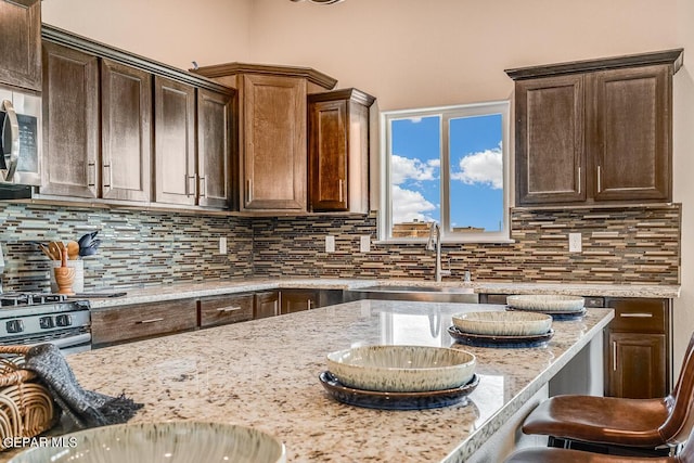 kitchen featuring light stone counters, stainless steel microwave, decorative backsplash, dark brown cabinetry, and a sink