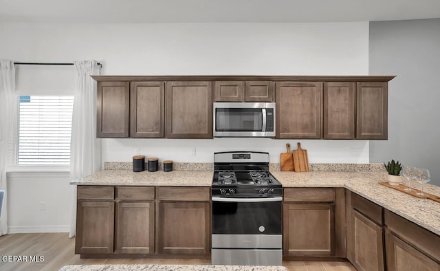 kitchen featuring appliances with stainless steel finishes, light stone counters, light wood-style flooring, and dark brown cabinetry