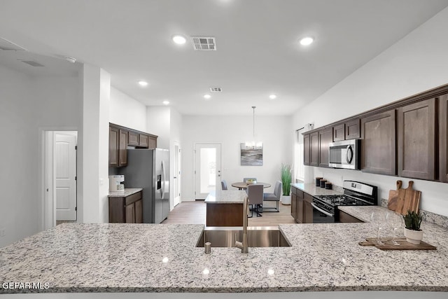 kitchen featuring stainless steel appliances, a sink, dark brown cabinets, light wood finished floors, and recessed lighting
