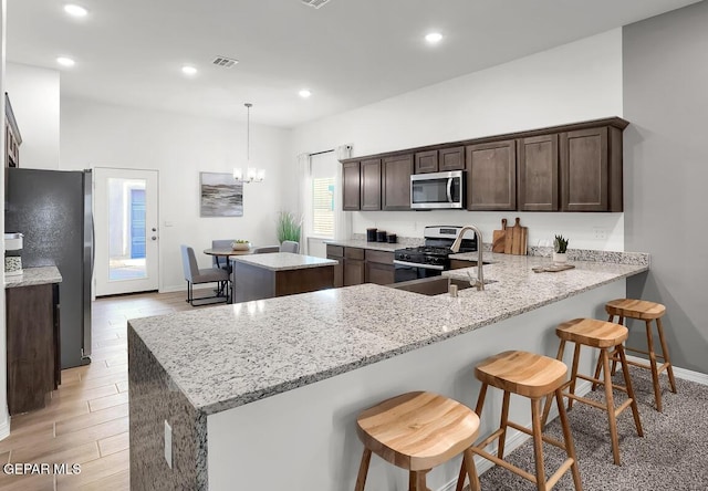 kitchen featuring appliances with stainless steel finishes, a center island, dark brown cabinetry, a peninsula, and light stone counters