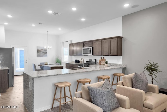 kitchen featuring stainless steel appliances, dark brown cabinetry, a peninsula, a chandelier, and a kitchen island
