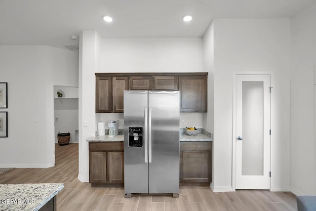 kitchen with stainless steel refrigerator with ice dispenser, light wood finished floors, dark brown cabinetry, light stone countertops, and baseboards