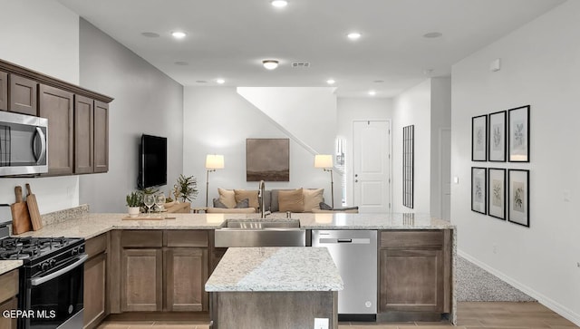 kitchen with stainless steel appliances, a sink, a peninsula, light wood finished floors, and light stone countertops