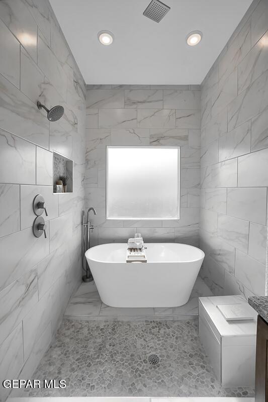 bathroom featuring marble finish flooring, recessed lighting, a freestanding bath, tiled shower, and tile walls