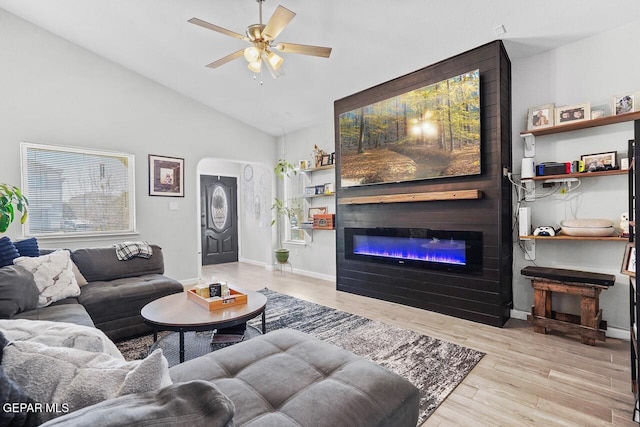 living area featuring wood finished floors, a ceiling fan, lofted ceiling, arched walkways, and a glass covered fireplace