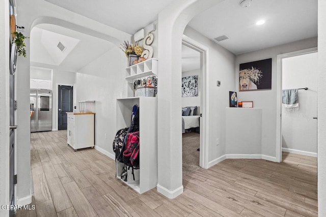 hall with visible vents, arched walkways, and light wood finished floors