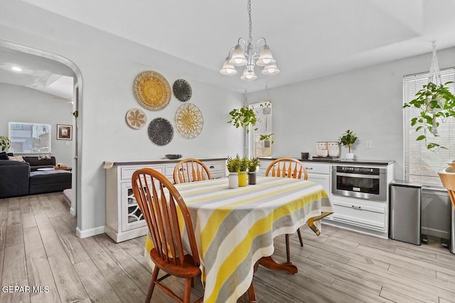 dining space featuring arched walkways, a chandelier, light wood-style flooring, and baseboards