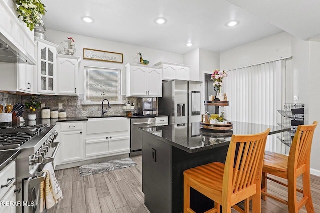 kitchen featuring ventilation hood, a kitchen breakfast bar, stainless steel appliances, white cabinetry, and a sink