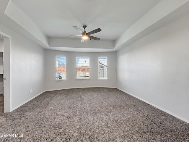 carpeted empty room featuring a raised ceiling, baseboards, and ceiling fan