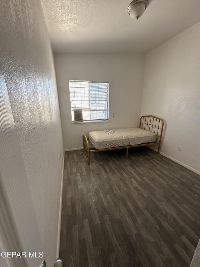 unfurnished bedroom featuring a textured wall, baseboards, dark wood-type flooring, and a textured ceiling