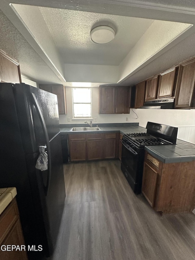 kitchen with black appliances, a sink, under cabinet range hood, a textured ceiling, and dark wood-style flooring