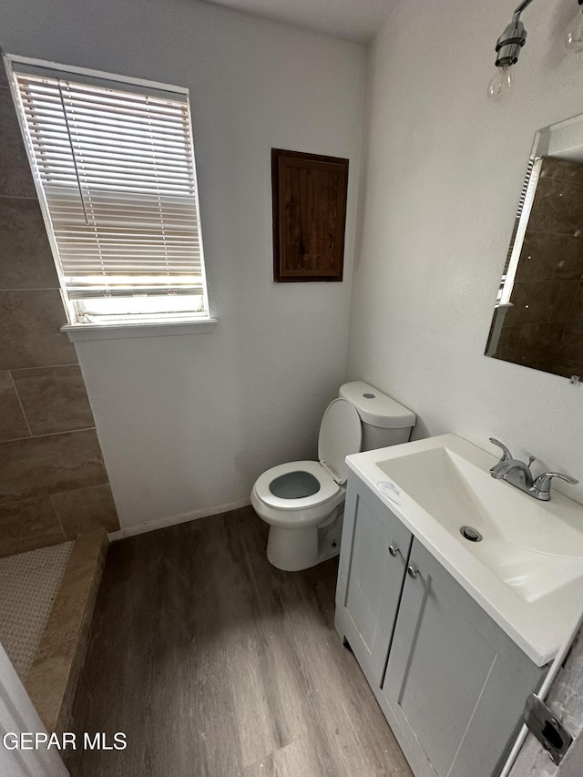 bathroom featuring toilet, wood finished floors, vanity, and a tile shower