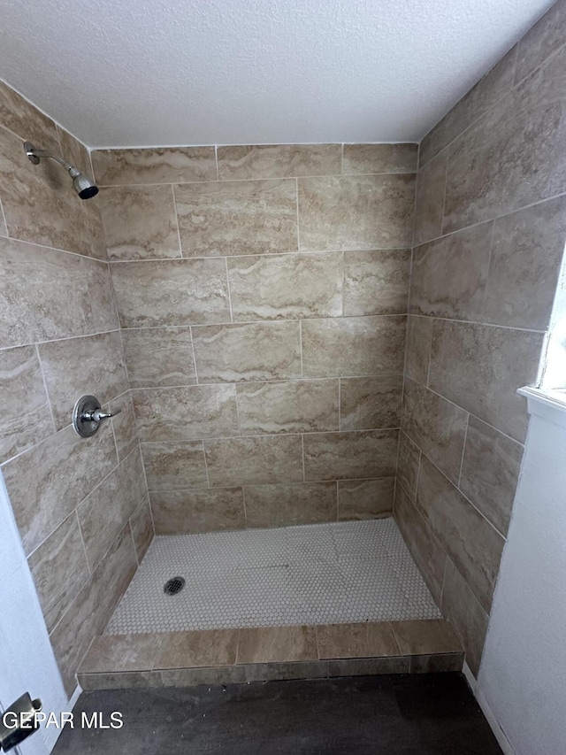 bathroom with a textured ceiling and tiled shower