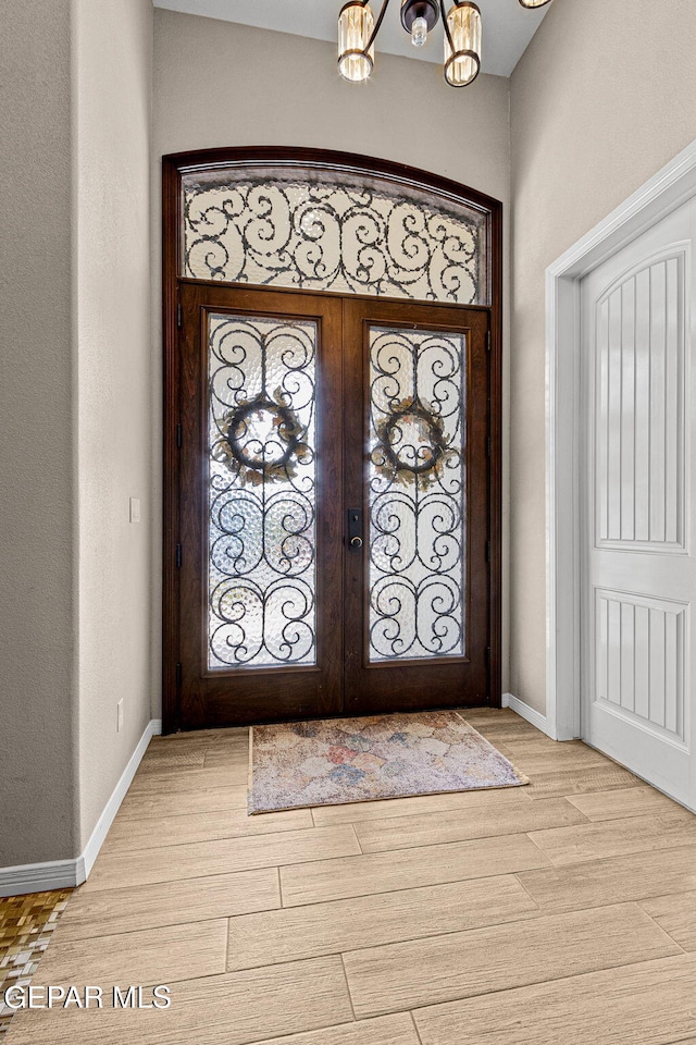 foyer with a chandelier, french doors, light wood-style flooring, and baseboards