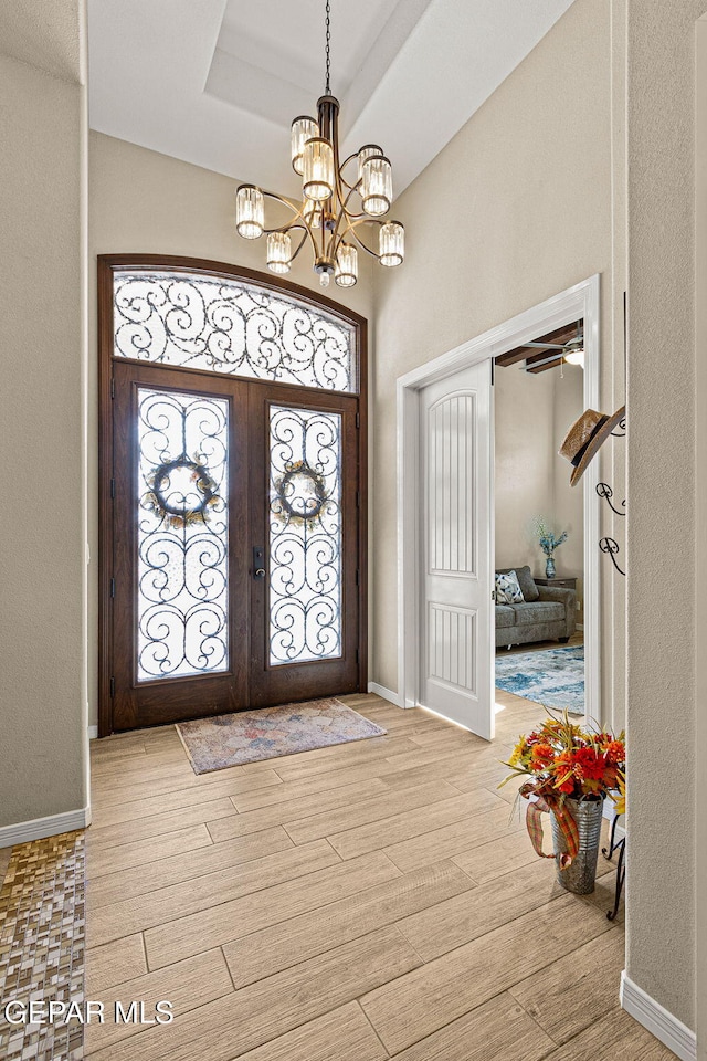 foyer entrance featuring a tray ceiling, french doors, an inviting chandelier, wood finished floors, and baseboards