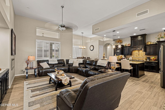 living area with visible vents, arched walkways, ceiling fan with notable chandelier, light wood-type flooring, and recessed lighting