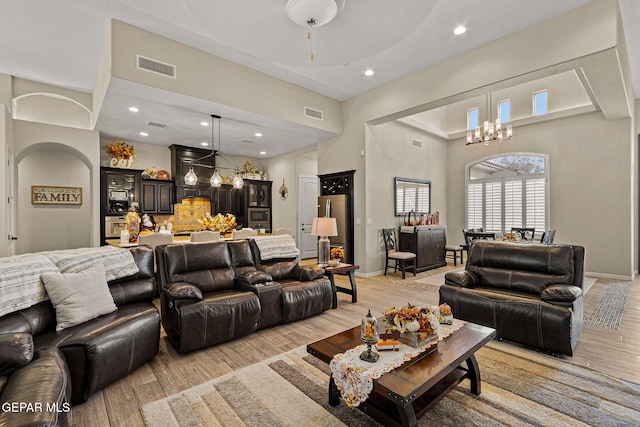 living area featuring baseboards, light wood-type flooring, visible vents, and an inviting chandelier