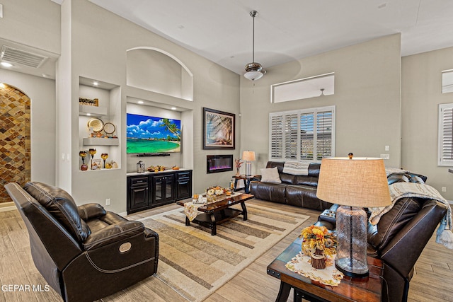 living area with visible vents, ceiling fan, a towering ceiling, and wood finished floors