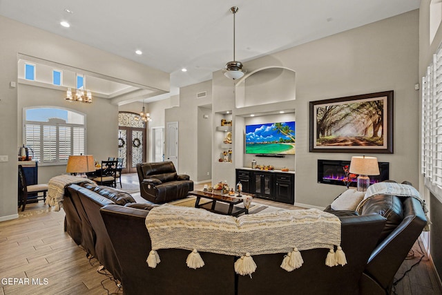 living area with wood finished floors, visible vents, baseboards, a glass covered fireplace, and an inviting chandelier