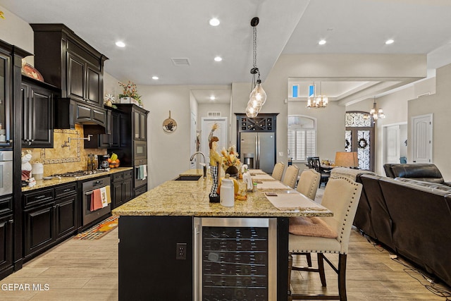 kitchen featuring appliances with stainless steel finishes, open floor plan, light wood-type flooring, beverage cooler, and a kitchen bar