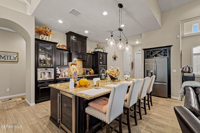 kitchen featuring light wood finished floors, stainless steel appliances, visible vents, beverage cooler, and a kitchen bar