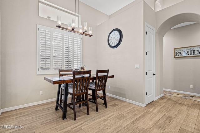 dining room featuring a chandelier, arched walkways, baseboards, and wood finished floors