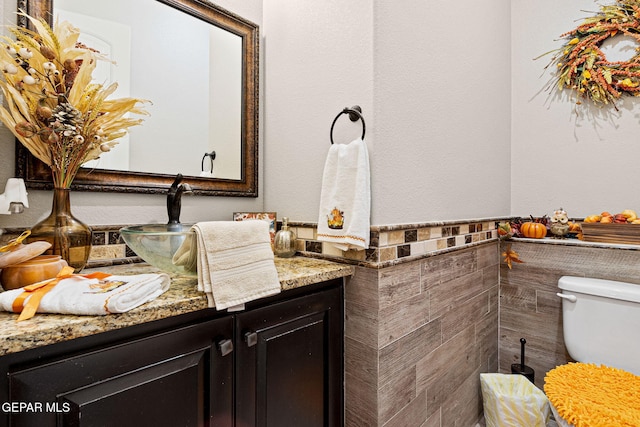 half bathroom featuring tile walls, wainscoting, vanity, and toilet