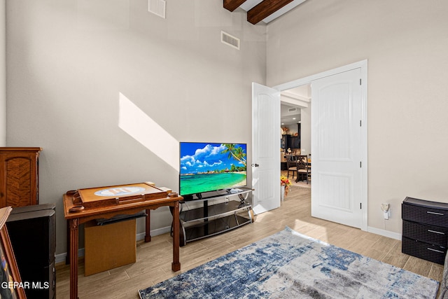 living area with baseboards, visible vents, beamed ceiling, and wood finish floors