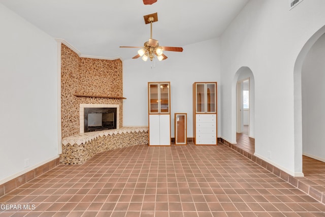 unfurnished living room featuring baseboards, arched walkways, ceiling fan, tile patterned floors, and a large fireplace