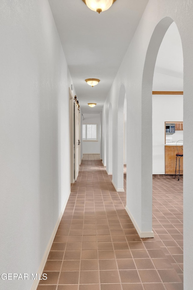 hall featuring baseboards, arched walkways, and tile patterned flooring