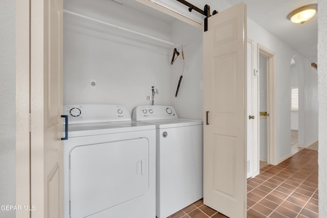 laundry area with tile patterned floors, washing machine and dryer, a barn door, arched walkways, and laundry area