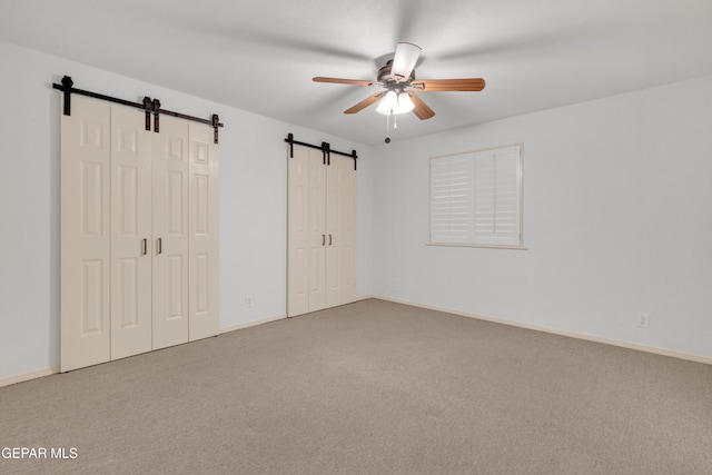 unfurnished bedroom with a ceiling fan, a barn door, carpet, and baseboards