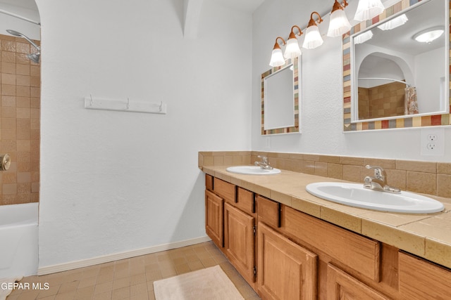 full bathroom with double vanity, shower / bath combo with shower curtain, baseboards, and a sink