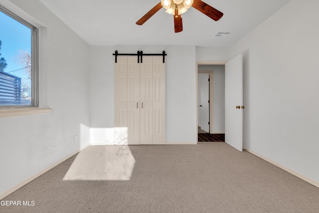 empty room featuring visible vents, ceiling fan, baseboards, a barn door, and carpet floors