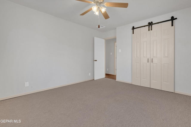 unfurnished bedroom with baseboards, a barn door, carpet flooring, a closet, and a ceiling fan