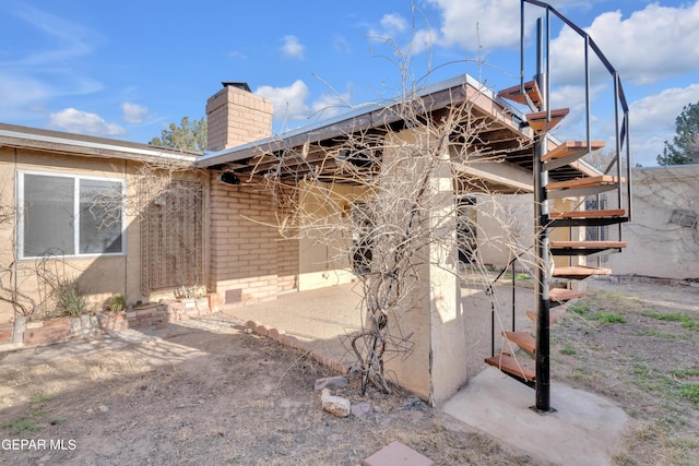 view of property exterior with stairs, crawl space, brick siding, a chimney, and a patio area